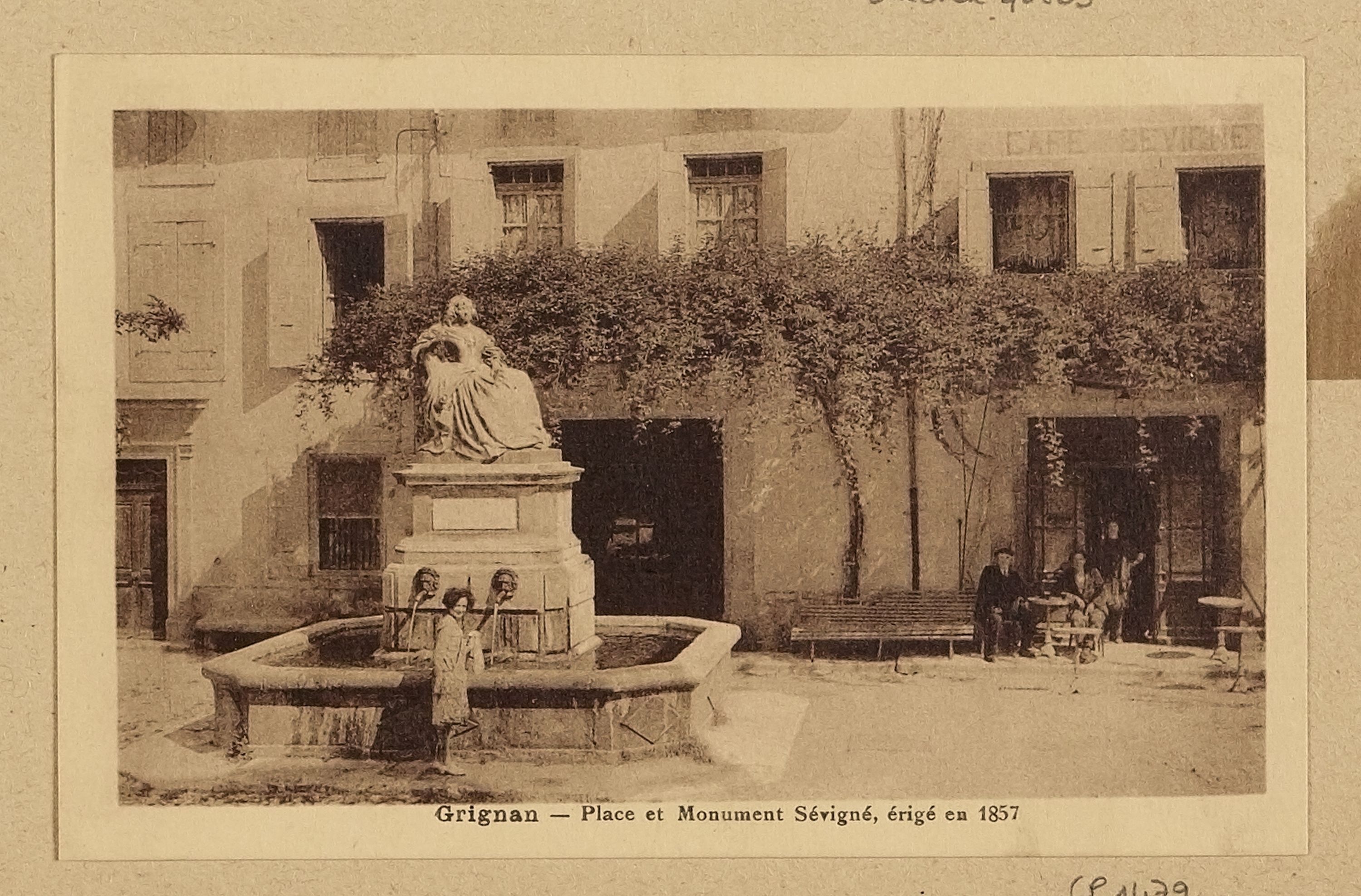 Ein altes Foto eines Brunnens mit einer Statue auf einem Sockel in der Mitte, umgeben von Menschen auf Bänken sitzend, mit einem Baum im Hintergrund und Text unten.
