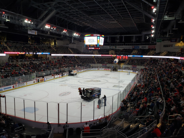 Eishockeyspiel in einer großen Arena mit Spielern auf dem Eis, Zuschauern in den Rängen, einem Fahrzeug auf dem Eis und dem Text 'New York Rangers vs Detroit Red Wings' auf den Tafeln.