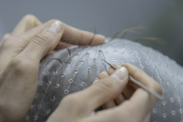 Eine Frau sitzt in einem Salon und lässt sich die Haare stylen, hält dabei eine Nadel und einen Faden in den Händen, mit einem unscharfen Hintergrund.