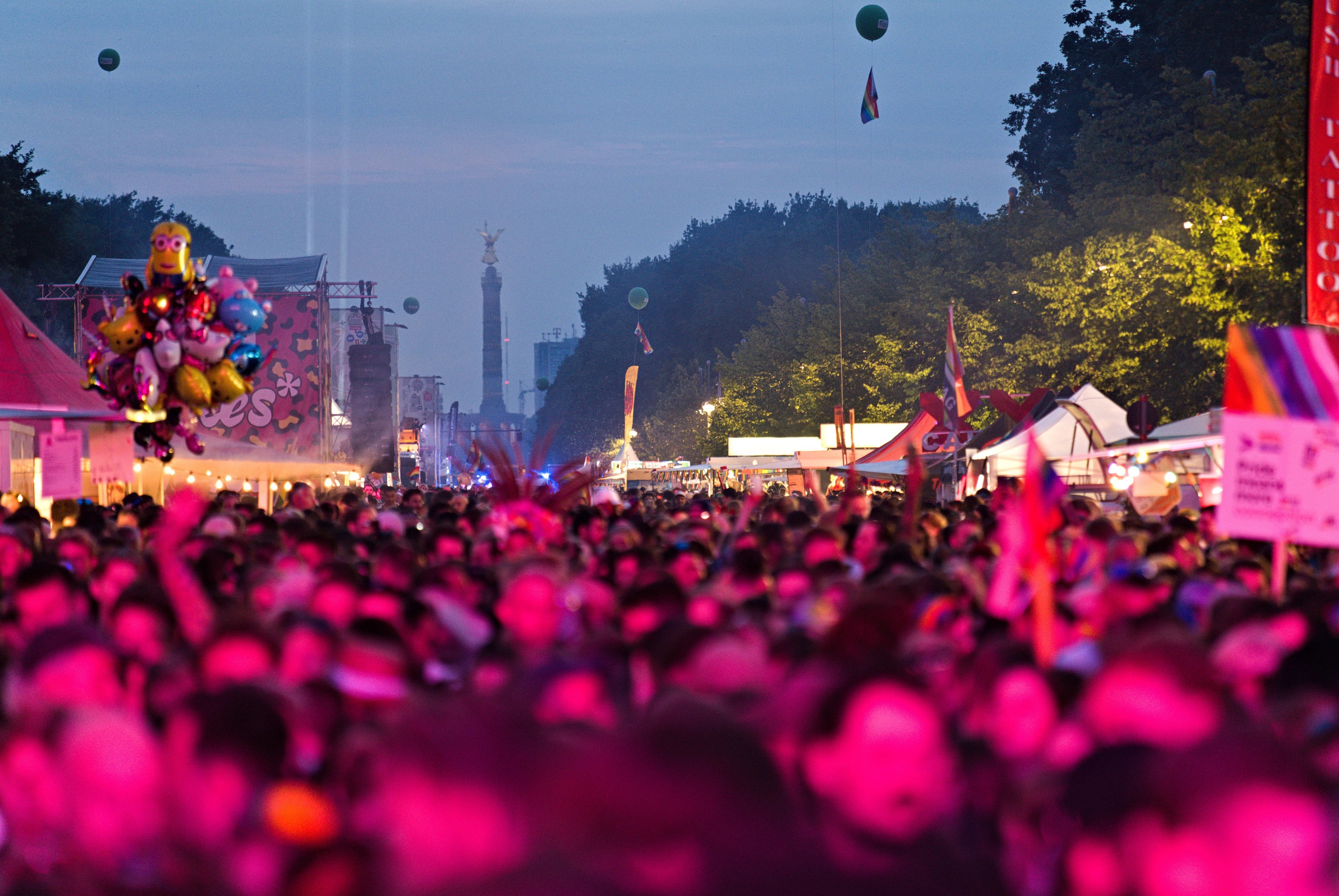 Eine große Menge bei einem nächtlichen Musikfestival mit bunten Lichtern, Ballons, Zelten, Bannern, Fahnen, Bäumen und einem sternenklaren Himmel im Hintergrund.