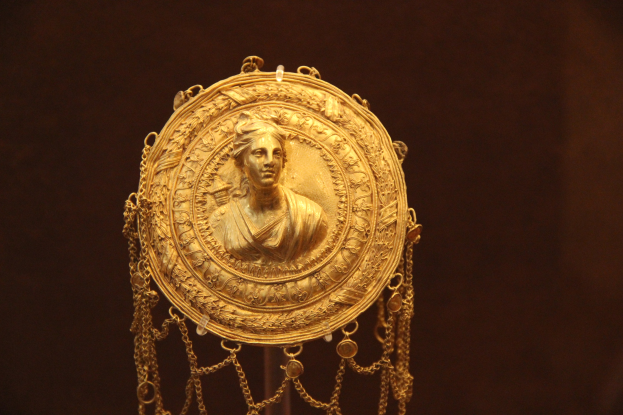 Goldene Medaille mit einer Frauengesicht, mit detaillierten Verzierungen auf dunklem Hintergrund.
