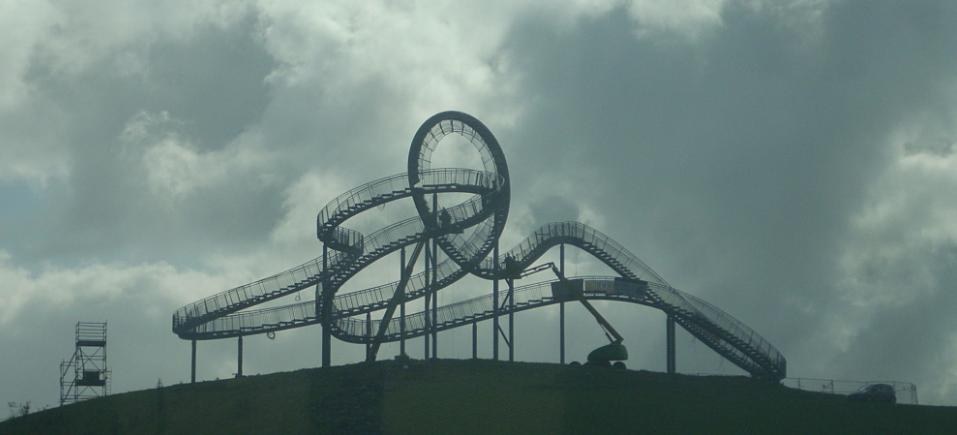 Eine Achterbahn auf dem Höhepunkt eines Hügels unter einem bewölkten Himmel mit Stützpfählen und -strukturen.