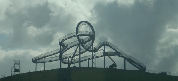 Eine Achterbahn auf dem Höhepunkt eines Hügels unter einem bewölkten Himmel mit Stützpfählen und -strukturen.