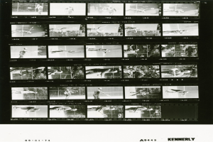 Schwarzes und weißes Foto eines Mannes in einem weißen Hemd und Shorts, der Tennis spielt und konzentriert eine Schläger hält, vor einem Filmstreifen-Hintergrund.