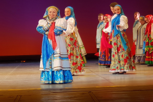 Eine Gruppe von Menschen in farbenfrohen, detaillierten traditionellen ukrainischen Kostümen, die fröhlich auf einer Bühne stehen.