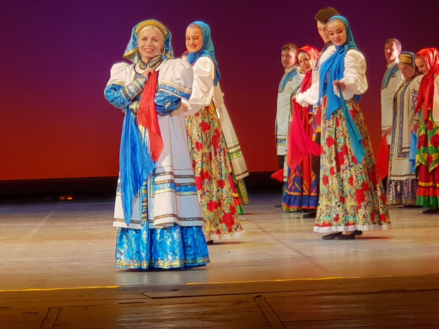 Eine Gruppe von Menschen in farbenfrohen, detaillierten traditionellen ukrainischen Kostümen, die fröhlich auf einer Bühne stehen.