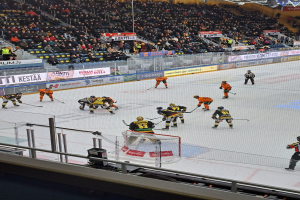 Menschen, die Hockey auf einem Eisstadion mit Zuschauern und Bannern im Hintergrund spielen.