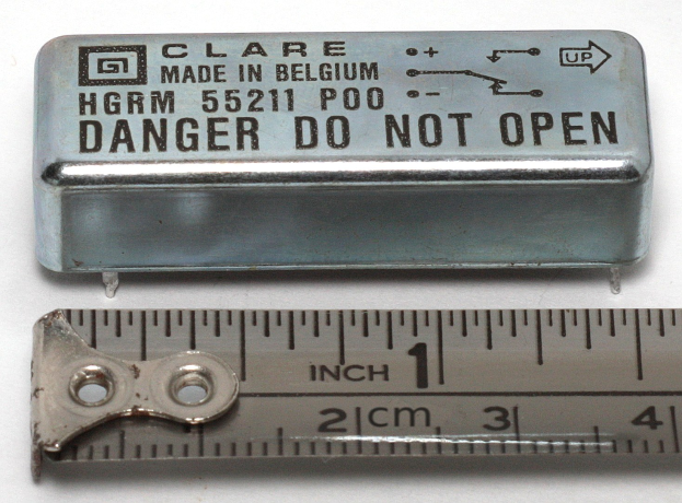 Metallbox mit der Aufschrift "Danger Do Not Open" neben einem Lineal auf einer weißen Oberfläche.