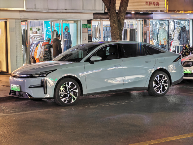Ein Mitsubishi Lancer EV Elektroauto auf einer Straße bei Nacht geparkt, umgeben von Gebäuden, Geschäften, Schaufensterpuppen, Schildern und Lichtern.