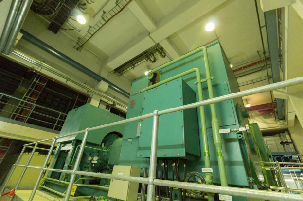 Großer industrieller Wärmetauscher in einem Gebäude, umgeben von Geländern, Rohren, Ventilen und Beleuchtungseinrichtungen.