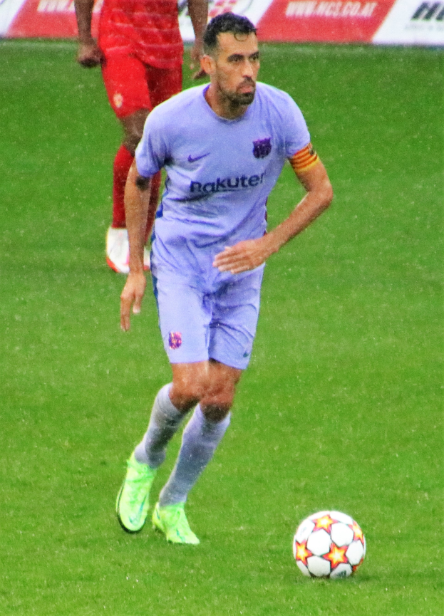 Ein Fußballer in einem Sportoutfit und -schuhen ist im Einsatz auf dem Feld, mit einer Texttafel im Hintergrund.