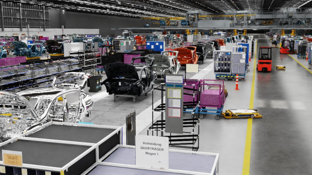 Große Fabrik mit mehreren Autos auf einer Fertigungsstraße, Metallstrukturen auf beiden Seiten, Fahrzeuge auf dem Boden, eine Wand im Hintergrund und an der Decke angebrachte Lampen; der Text legt nahe, dass es sich um eine Volkswagen-Fabrik in Deutschland handelt.