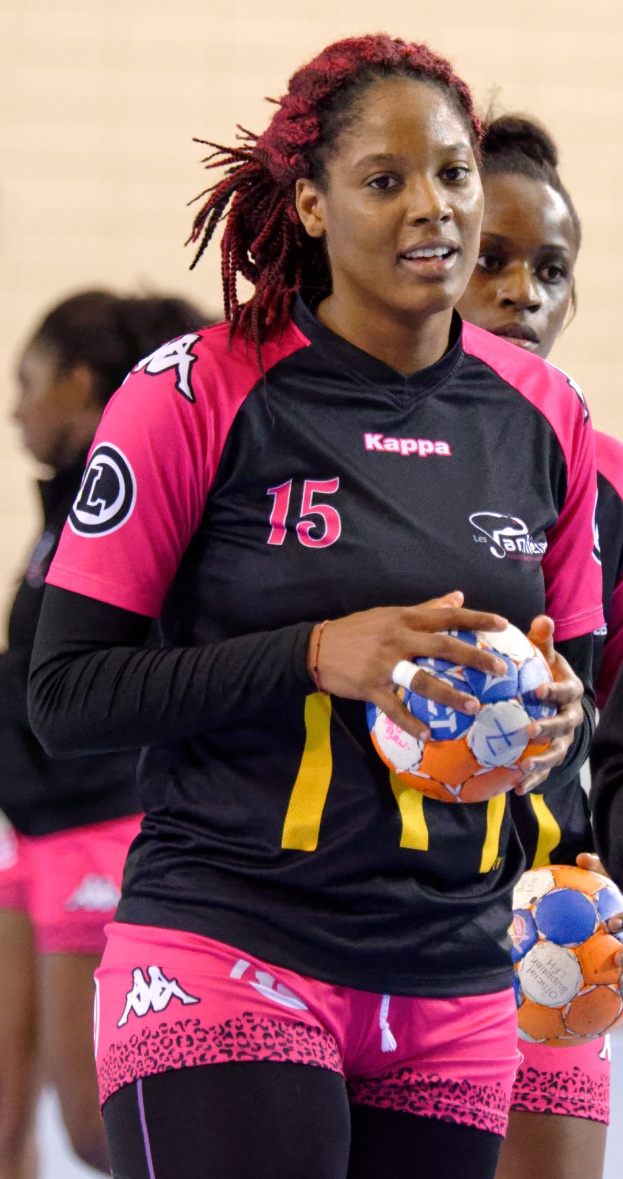 Eine Gruppe von Frauen, die zusammenstehen, jede einen Fußball haltend, wobei die Frau in der Mitte ein menschliches Gesicht hat, direkt in die Kamera schaut, ein weißes T-Shirt und blaue Shorts trägt.