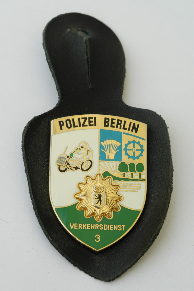 Ein schildförmiges Polizeisiegel mit der Aufschrift "Polizei Berlin" in schwarzer fetter Schrift, das ein weißes Stern auf einem blauen Hintergrund und einen weißen Rand hat, auf einer Oberfläche platziert.