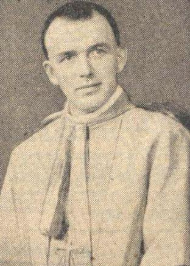 Ein Schwarz-Weiß-Foto eines Mannes in Priesterkleidung, der eine weiße Robe mit schwarzem Kragen und Manschetten und eine schwarze Mütze mit einer weißen Feder trägt, mit gefalteten Händen und einem ernsten Gesichtsausdruck.