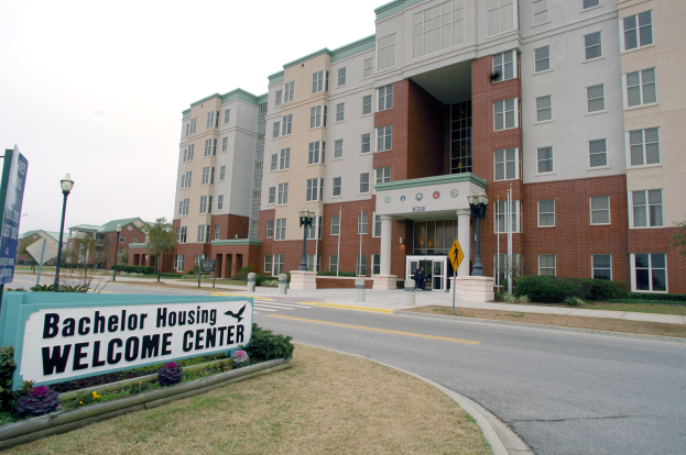 Außenansicht des Bachelor-Housing-Willkommenszentrums mit Gebäuden, Straßenmöbeln, Fahrzeugen, Grünflächen und einem klaren Himmel.