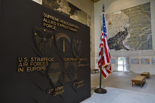 Eintritt zum Hauptquartier der US-Strategischen Luftstreitkräfte in Europa mit einer amerikanischen Flagge, Text und Logos an der Wand, Bänken, einer Tafel, Fotorahmen, beleuchteter Decke und einer Tür im Hintergrund.