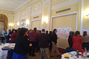 Eine Gruppe von Menschen untersucht Plakate und Diagramme, die an einer Wand zu sein scheinen, die ein Kunstmuseum zu sein scheint.