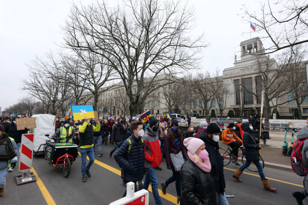 Ein großer Protestmarsch in Washington, D.C. am 21. Januar 2020 mit Menschen, die Plakate und Schilder halten und Fahrräder fahren, vor einem Gebäude auf einer Straße unter einem klaren blauen Himmel mit Bäumen und Schildern im Hintergrund.
