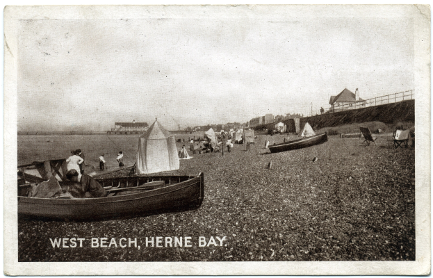 Schwarz-weiß-Foto von Menschen am Weststrand, Herne Bay, mit Booten im Vordergrund, H├Ąusern und einem Zaun im Hintergrund und Text unten.