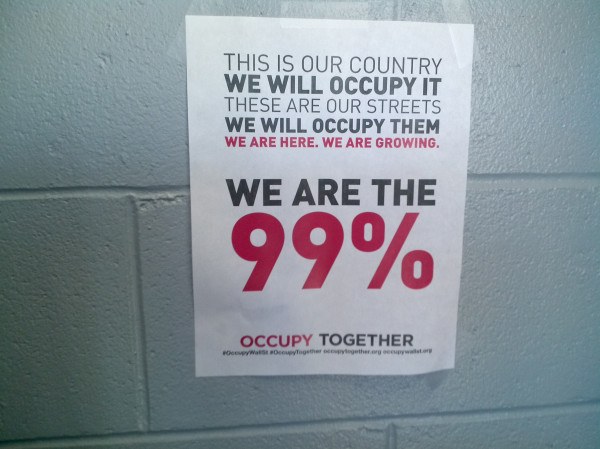 Plakat an einer Wand mit fetter schwarzer Schrift, die "Occupy Wall Street" und "Wir sind die 99%." lautet.