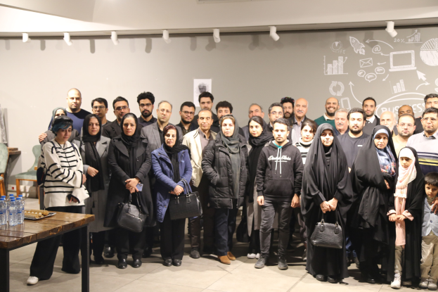 Eine Gruppe von Muslim-Gemeindemitgliedern steht vor einem Tisch mit Wasserflaschen und anderen Gegenständen, mit einer Wandtafel im Hintergrund und Deckenbeleuchtung.