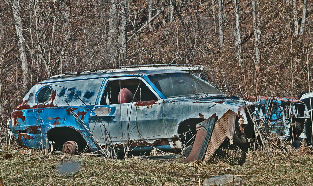 Abandoned vehicles and metal items on the ground with bare trees in the background.