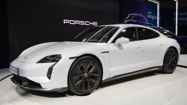 Weißer Porsche Taycan Turbo S E-Hybrid auf der IAA gezeigt, umgeben von schwarzen Schlafzimmermöbeln in einem modernen Zuhause.