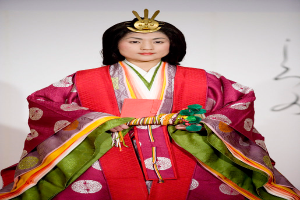 Eine Frau in einem traditionellen japanischen Kimono, das ein leuchtendes rotes und grünes Kleid mit aufwändigen Mustern trägt, steht selbstbewusst auf einem Laufsteg.