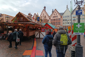 Menschen auf einem Kopfsteinpflasterweg neben einem Weihnachtsmarkt in Nürnberg, Deutschland, mit Laternenmasten und Informationsschildern im Hintergrund.