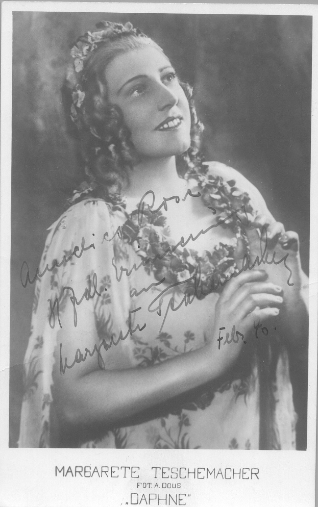 Ein Schwarz-Weiß-Foto einer Frau in einem Kleid mit einem klassischen 1940er-Jahre-Hairstyle, die warm lächelt mit leuchtenden Augen und leicht geöffneten Lippen.