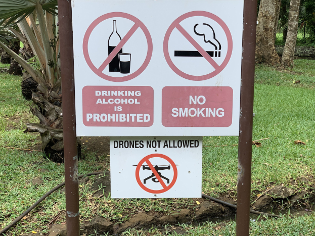 Schilder am Straßenrand mit der Aufschrift "Alkoholtrinken ist verboten" und "Rauchen verboten" mit Bäumen und Gras im Hintergrund.
