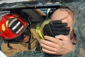 Ein Feuerwehrmann mit Helm und Handschuhen inspiziert ein Auto durch ein zerbrochenes Fenster.