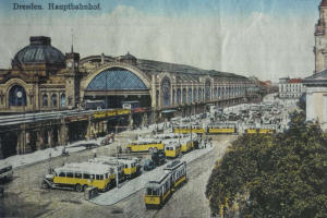 Eine alte Ansichtskarte zeigt einen belebten Dresdner Bahnhof mit Fahrzeugen, Menschen, Bäumen, Gebäuden und einem bewölkten Himmel, mit der Aufschrift "Dresden Hauptbahnhof" oben.