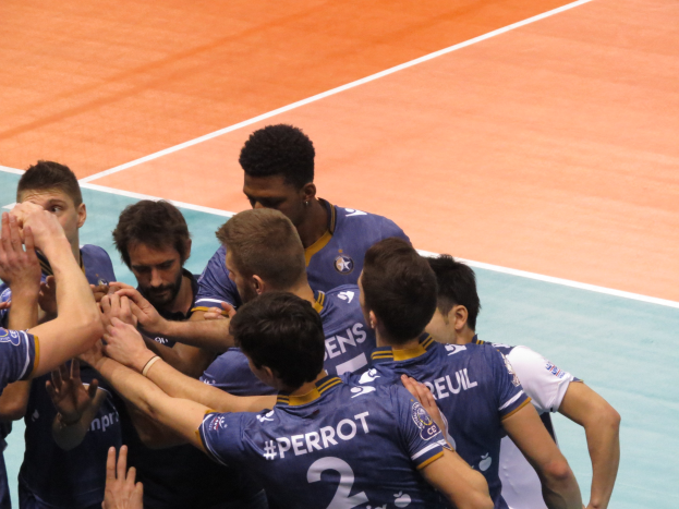 Eine Gruppe von Männern in blauen "Ligue 1"-T-Shirts feiert auf einem Volleyballfeld und reckt die Hände in die Luft.