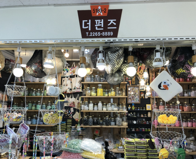Ein Ladeneinrichtungsbild mit verschiedenen Gegenständen wie Körbchen, Lichtern, Flaschen und Spielzeugen, die auf Regalen angeordnet sind und ein Schild öber dem Eingang, das es als bestes koreanisches Geschäft in Seoul ausweist.