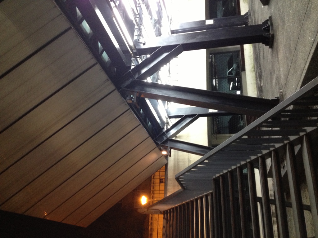 Treppen mit Geländern in der rechten unteren Ecke, Säulen auf der rechten Seite des Bodens, Autos in Gebäuden hinter den Säulen und Lampen auf der linken Seite mit einer sichtbaren Decke.