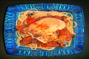 Ein blaues Teller mit Spaghetti und Hühnerjagd, das eine großzügige Portion Spaghetti, gekochtes Huhn und eine reichhaltige Tomatensauce enthält.
