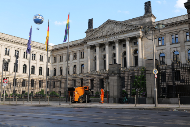 Großes modernes Regierungsgebäude mit vielen Fenstern, umgeben von Straßenmöbeln und Fahrzeugen, mit der Flagge des Deutschen Bundestags