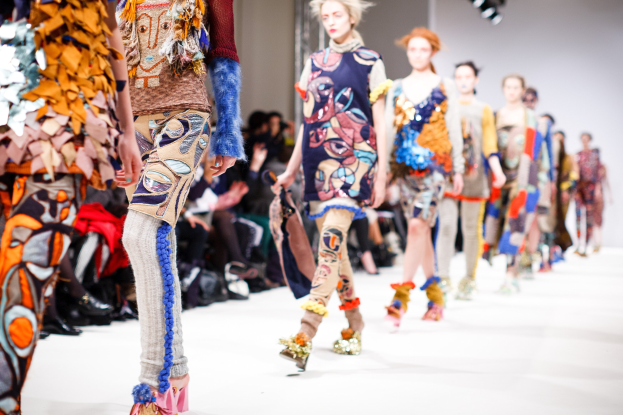 Eine Gruppe Von Frauen, Die Eine Laufsteg In London Fashion Week Heruntergehen, Mit Einem Publikum, Das Im Hintergrund Sitzt, Unter Hellen Lichtern.