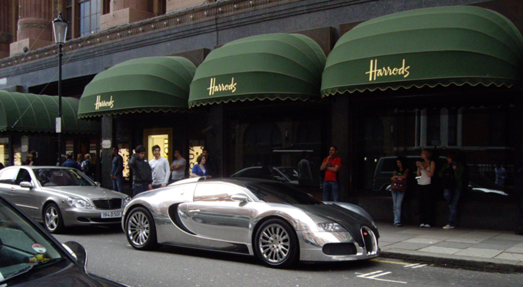 Eine Straße mit Autos, Menschen, die daruntergehen, und einem Laternenmast zur Seite.