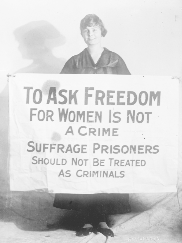 Schwarz-weiß-Fotografie einer Frau, die ein Banner hält, auf dem steht: "Für die Freiheit der Frauen zu kämpfen, ist kein Verbrechen, Suffragetten sollten nicht wie Kriminelle behandelt werden."