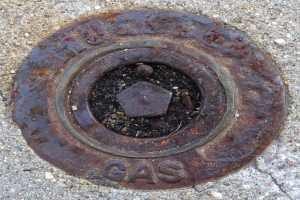 Rostiger Metall-Schachtobdeckel auf dem Boden mit dem Wort "Gas" darauf