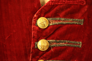 Nahaufnahme einer roten Samtjacke mit goldenen Knöpfen, die einen luxuriösen und eleganten Eindruck vermittelt.