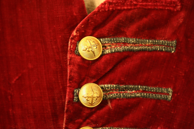 Nahaufnahme einer roten Samtjacke mit goldenen Knöpfen, die einen luxuriösen und eleganten Eindruck vermittelt.