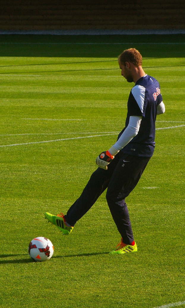 Ein Mann in einem Fußballtrikot kickt einen Fußball auf einem Fußballfeld und sieht entschlossen aus.