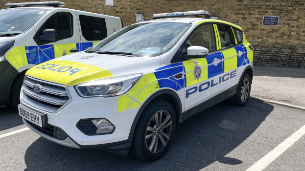 Zwei Polizeiwagen nebeneinander auf einem Parkplatz geparkt mit einer Wandtafel im Hintergrund, die eine Polizeiermittlung anzeigt.