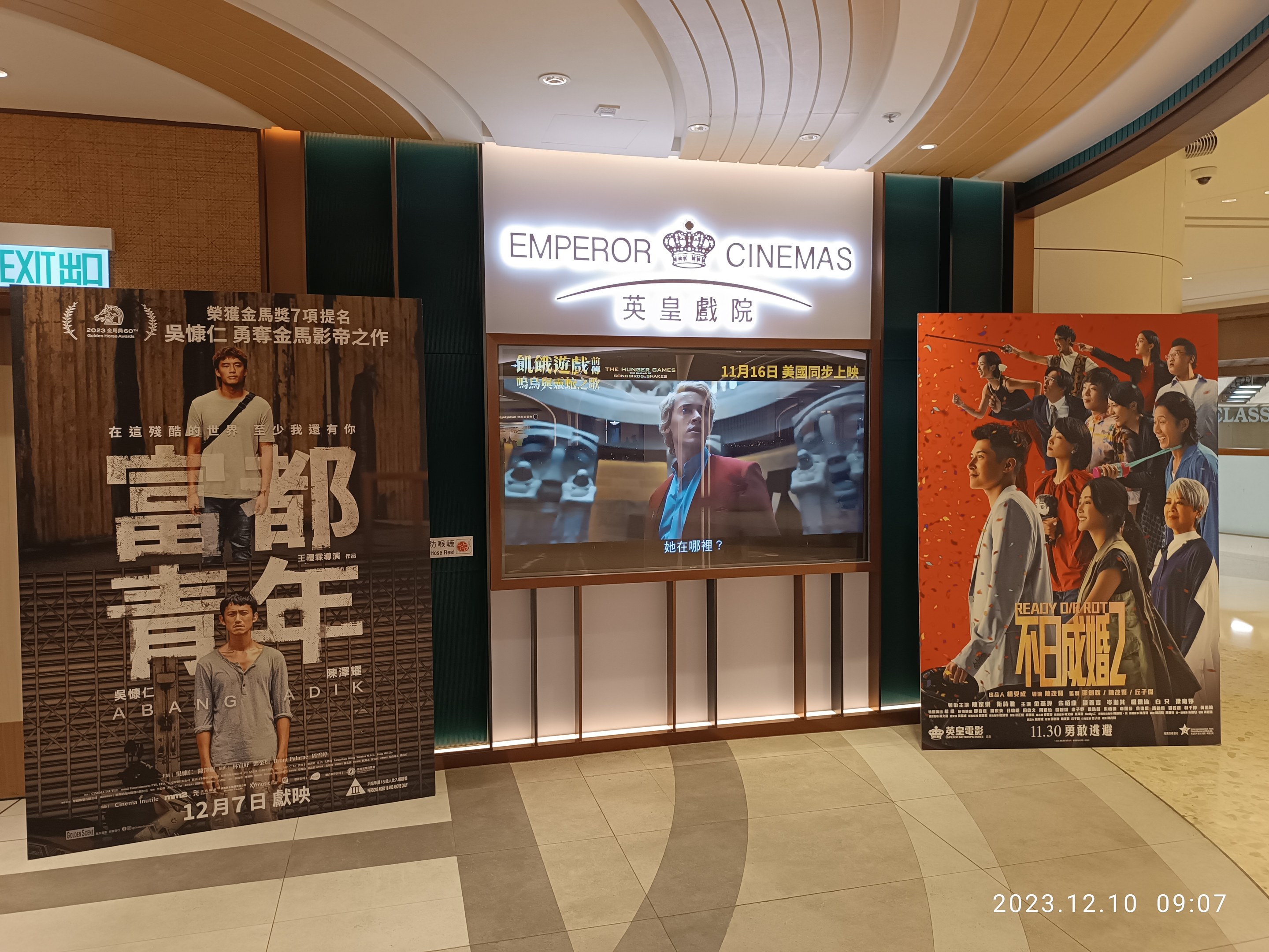 Eintritt zum Emperor Cinemas in Hong Kong mit Bannern, einem Bildschirm, einer Namensplakette, Deckenleuchten und einem Wasserzeichen.