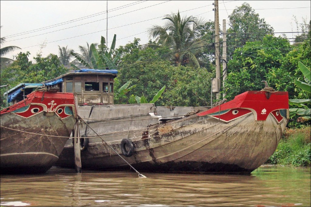Zwei Bootshäuser auf dem Wasser mit zahlreichen Bäumen im Hintergrund und zwei Strommasten mit vielen Drähten vor den Bäumen.