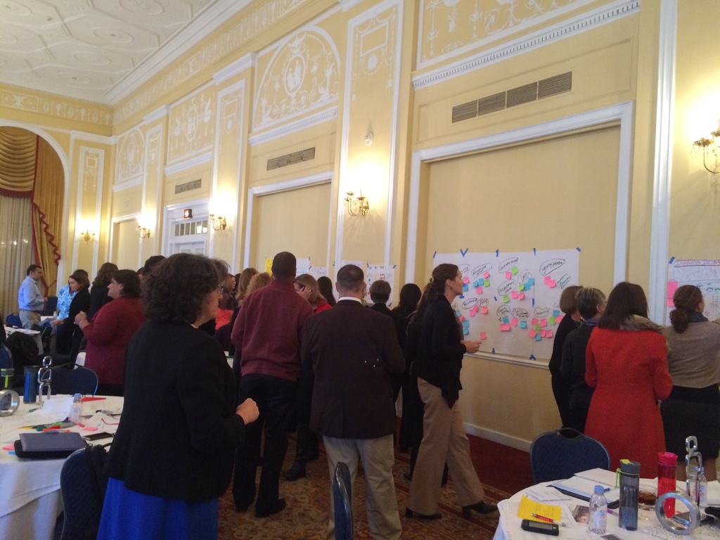 Eine Gruppe von Menschen betrachtet Plakate und Charts an einer Wand in einem Raum, der wie ein Kunstmuseum aussieht.